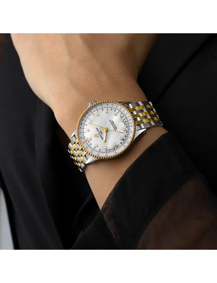 Breitling Navitimer Chronometer wristwatch with a 18k yellow gold and steel case and bracelet, mother-of-pearl dial, and diamond hour markers with gold hands on a wrist with a black sleeve in the background.