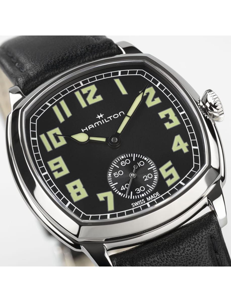Close-up of a Hamilton wristwatch with a black dial, large luminescent numerals, and a small seconds subdial, mounted on a black leather strap.