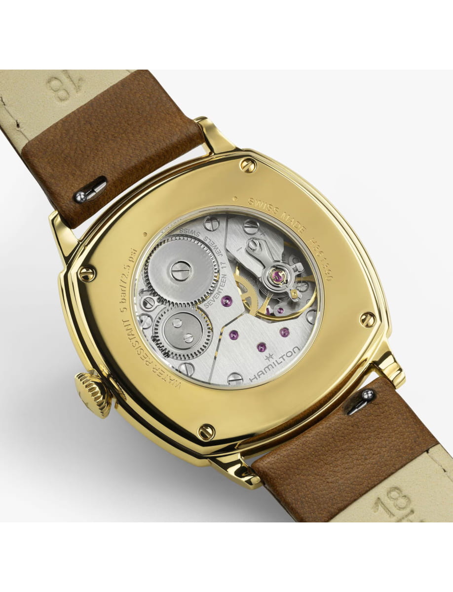 Gold-toned watch back with a transparent case revealing the inner mechanical movement and jewel bearings, paired with a brown leather strap