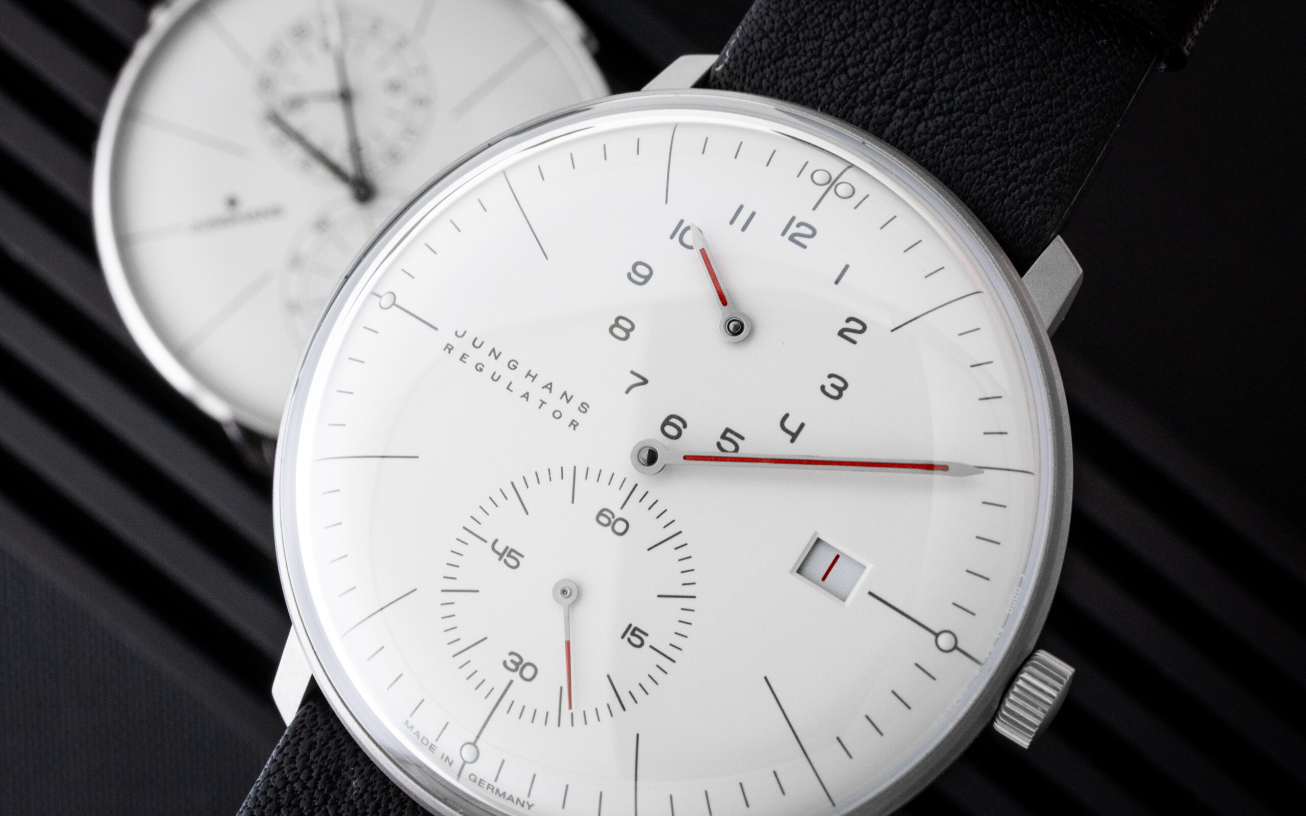 Close-up of a white dial wristwatch with black numerals, red hands, and a textured black strap.