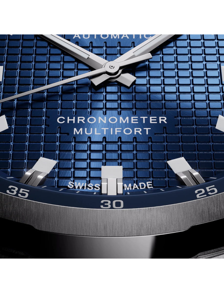 Close-up of a Mido blue watch dial with silver hands, showing 'CHRONOMETER MULTIFORT' and 'SWISS MADE'.