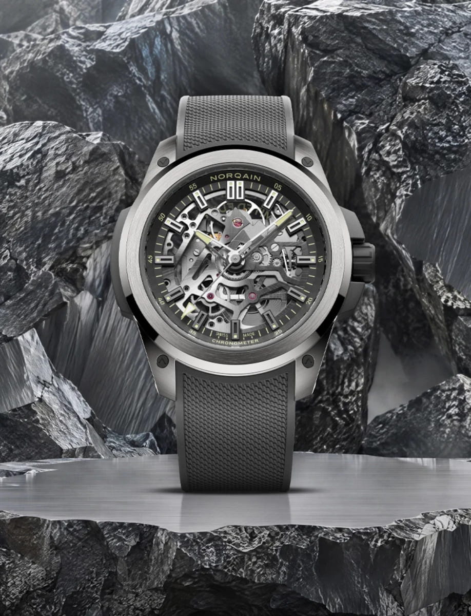 Norqain skeleton wristwatch with visible gears and black dial, gray strap, titanium Grade 5 case displayed on a rocky pedestal backdrop.