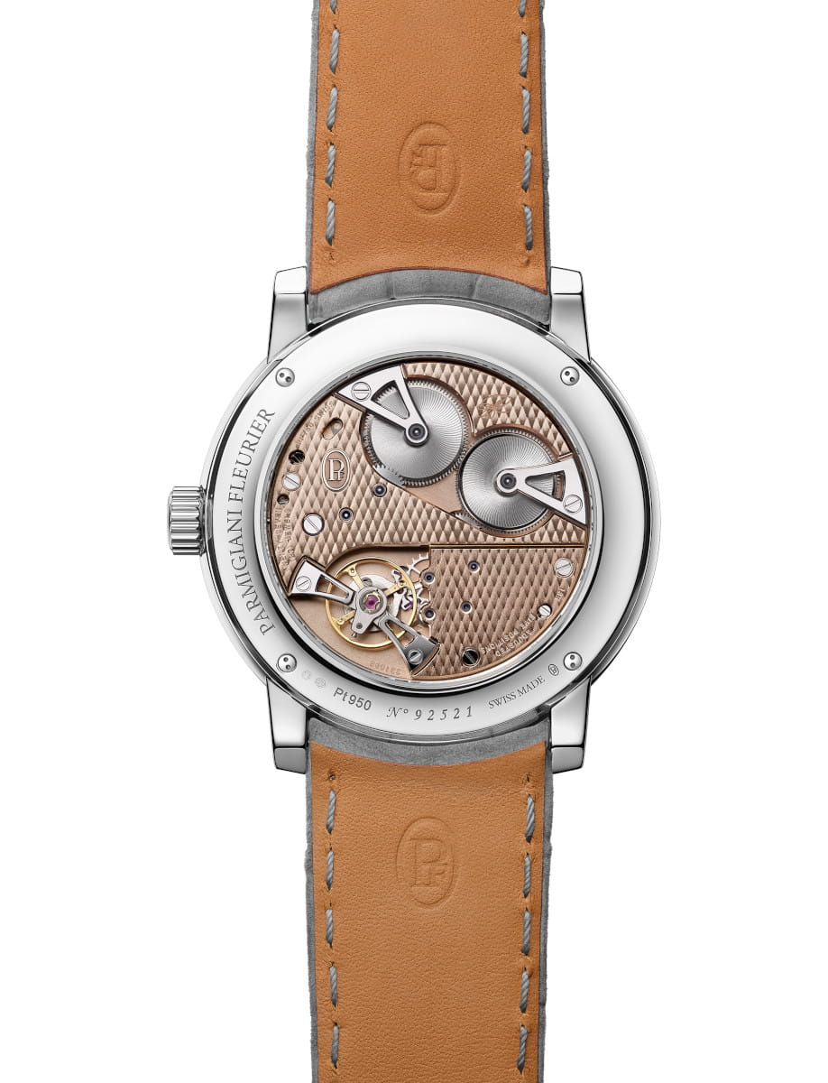 Back of a Parmigiani Fleurier wristwatch showing a rose-gold guilloché movement through a transparent caseback and tan leather strap.