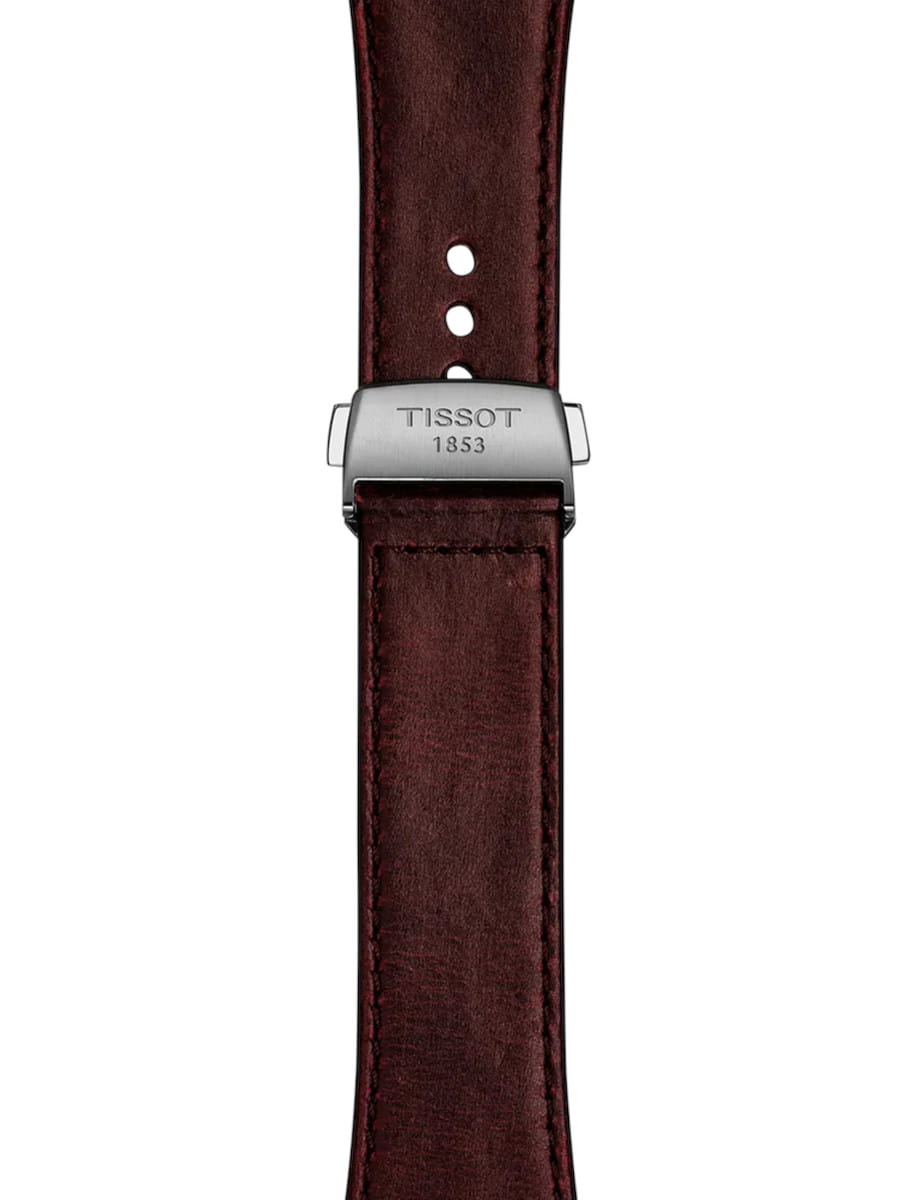 Close-up of a burgundy leather watch strap with a steel clasp engraved 'TISSOT 1853'.